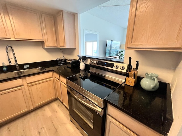 kitchen featuring electric range, light wood-type flooring, dark stone countertops, a sink, and light brown cabinets