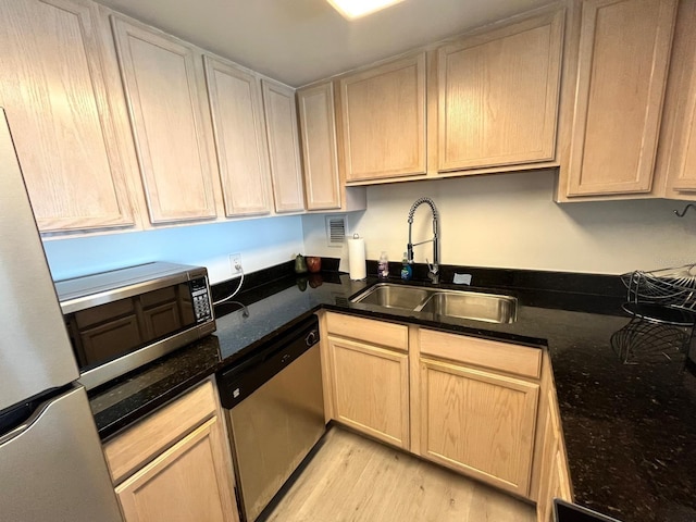 kitchen featuring a sink, appliances with stainless steel finishes, light brown cabinetry, light wood finished floors, and dark stone counters