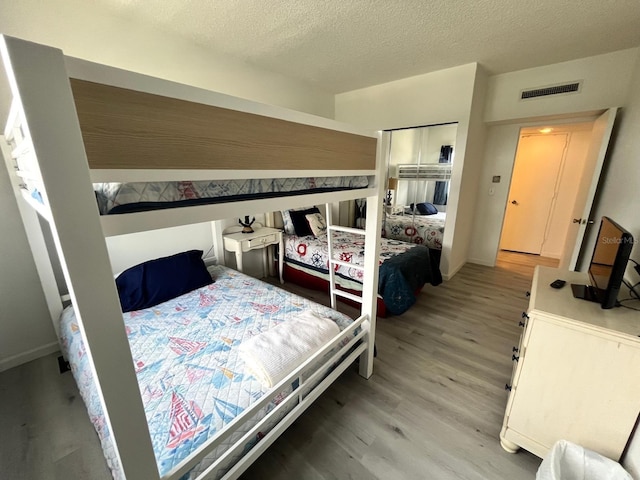 bedroom with visible vents, light wood-type flooring, and a textured ceiling