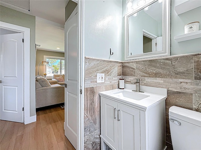 ensuite bathroom with wood finished floors, tile walls, toilet, ensuite bathroom, and vanity