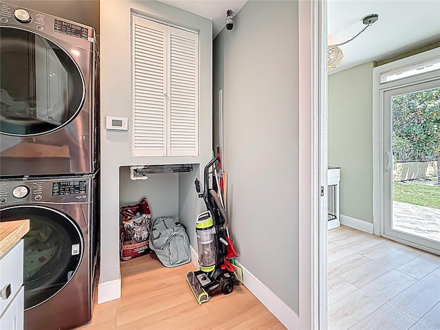 laundry room featuring wood finished floors, stacked washer / drying machine, laundry area, and baseboards