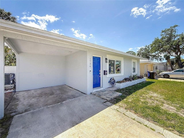 view of front of home featuring a front yard, central air condition unit, stucco siding, and concrete driveway