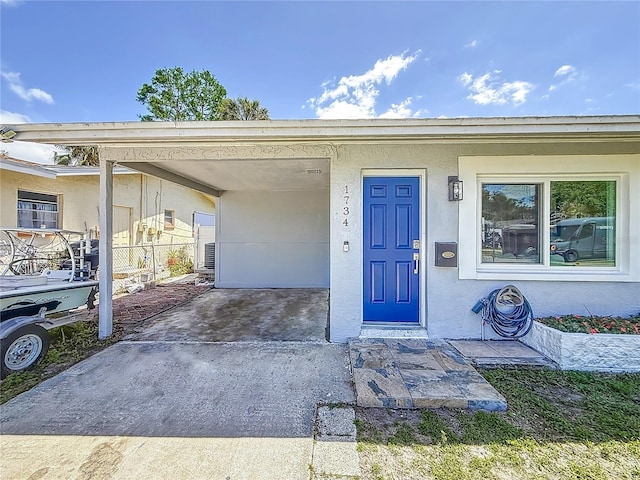 doorway to property featuring an attached carport, driveway, and stucco siding