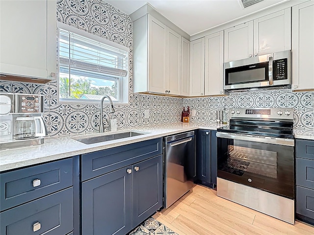 kitchen featuring a sink, light wood-type flooring, tasteful backsplash, light countertops, and appliances with stainless steel finishes