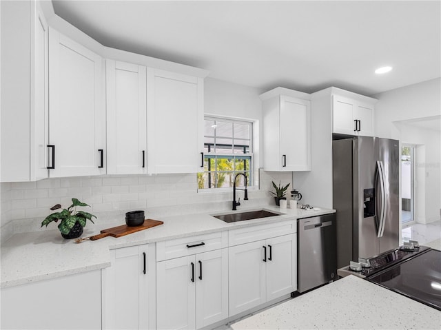 kitchen featuring light stone countertops, tasteful backsplash, white cabinetry, appliances with stainless steel finishes, and a sink