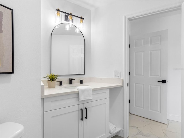 bathroom with toilet, marble finish floor, vanity, and baseboards