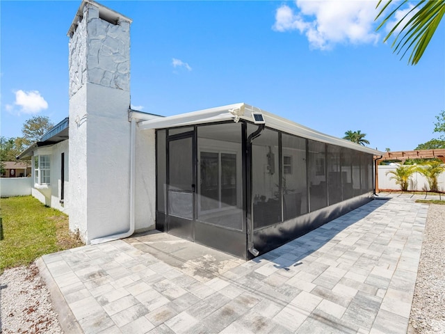 rear view of property featuring a sunroom, a patio, stucco siding, and fence