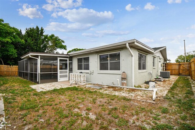 rear view of property with central air condition unit, a fenced backyard, a sunroom, and stucco siding