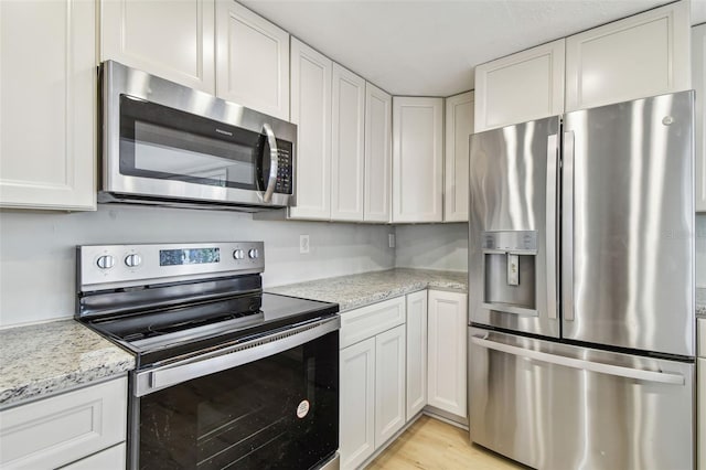 kitchen with light wood-style floors, appliances with stainless steel finishes, light stone counters, and white cabinetry