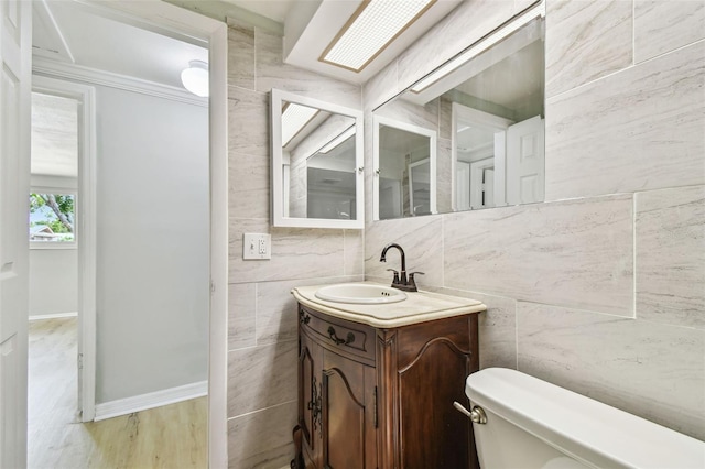 half bath featuring toilet, baseboards, tile walls, and vanity