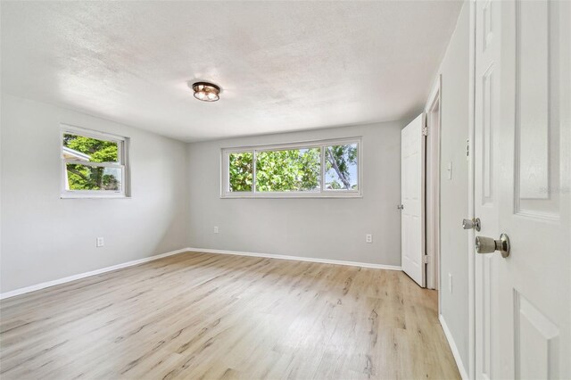 unfurnished bedroom with baseboards, a textured ceiling, light wood finished floors, and multiple windows