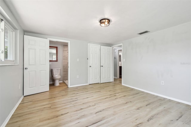 unfurnished bedroom with visible vents, baseboards, ensuite bathroom, and wood finished floors