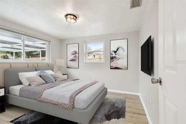 bedroom with baseboards, multiple windows, light wood-style flooring, and visible vents