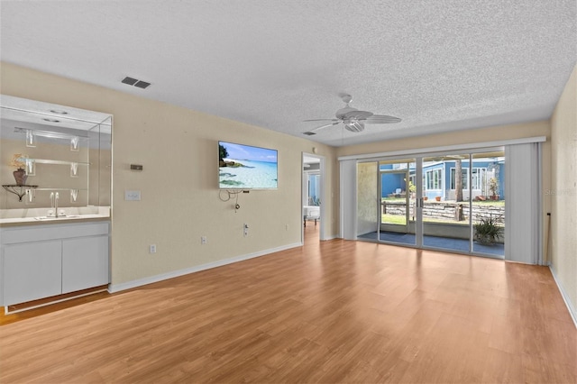 2023 Golfview Dr Unit 2023, Tarpon Springs, FL 34689 - unfurnished living room featuring light wood-type flooring, a textured ceiling, ceiling fan, baseboards, and bar with sink