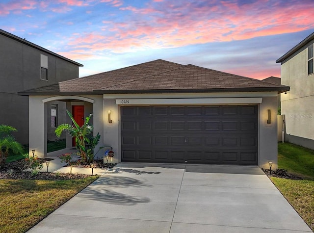view of front of home featuring roof with shingles, an attached garage, driveway, and stucco siding
