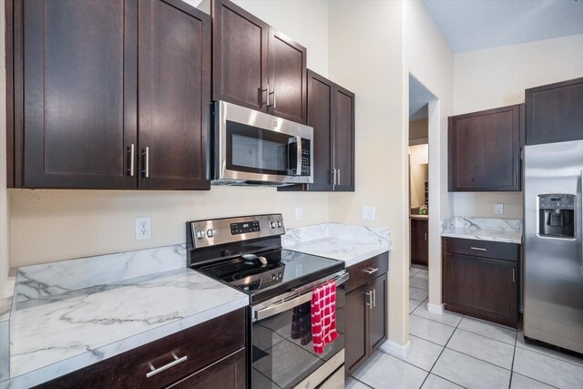 kitchen featuring light stone countertops, dark brown cabinetry, light tile patterned flooring, and appliances with stainless steel finishes