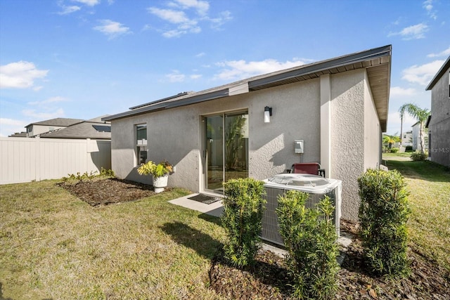 back of house featuring a yard, stucco siding, fence, and central AC
