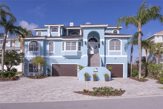 coastal inspired home featuring decorative driveway, a garage, stucco siding, and stairway