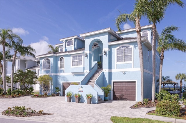 beach home with stucco siding, decorative driveway, stairs, and a garage