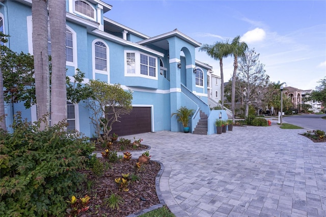 view of front of house featuring stucco siding, decorative driveway, stairs, and an attached garage