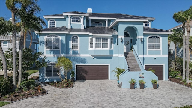 raised beach house featuring stucco siding, decorative driveway, and an attached garage