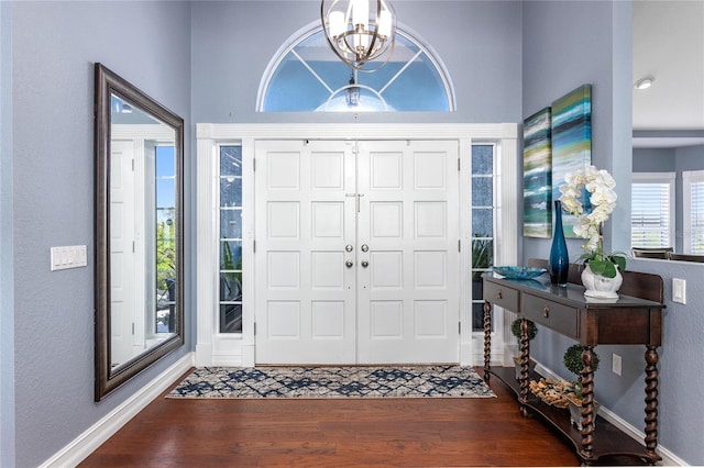 foyer entrance with a notable chandelier, wood finished floors, a textured wall, and baseboards