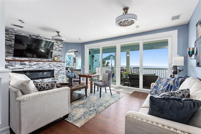 living area with wood finished floors, visible vents, a stone fireplace, and arched walkways