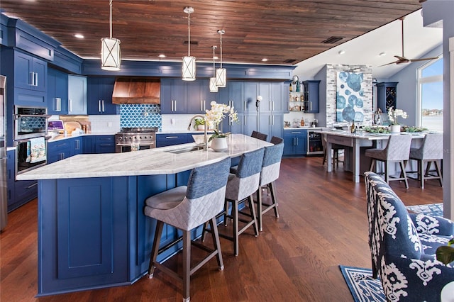 kitchen with a sink, wooden ceiling, stainless steel appliances, custom range hood, and blue cabinets