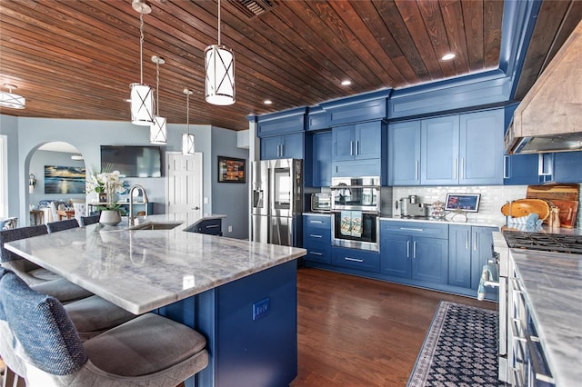 kitchen with arched walkways, wood ceiling, appliances with stainless steel finishes, wall chimney range hood, and a sink