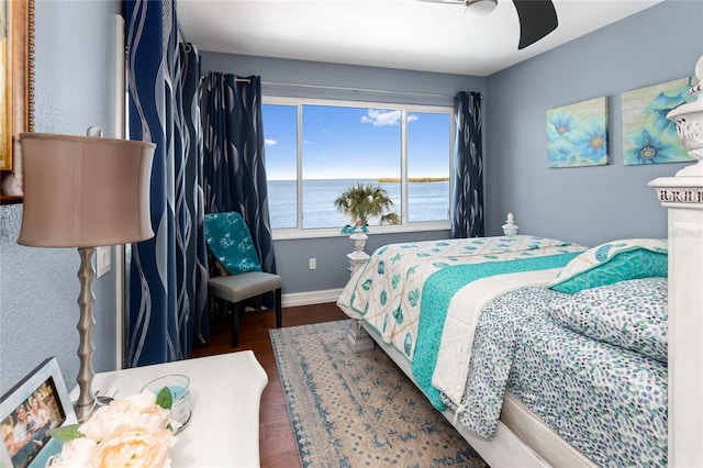 bedroom with a ceiling fan, a water view, wood finished floors, and baseboards