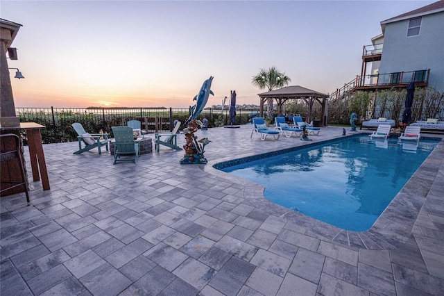pool at dusk featuring a fenced backyard, a gazebo, a patio area, and a fenced in pool
