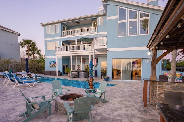 rear view of house with a balcony, a patio, a jacuzzi, a fenced in pool, and an outdoor fire pit