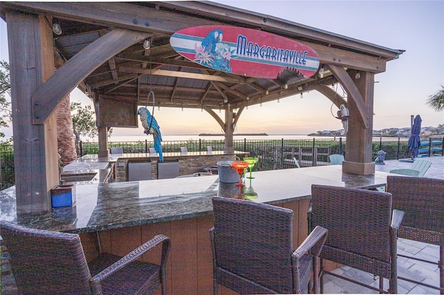 view of patio featuring fence, a gazebo, a water view, outdoor wet bar, and exterior kitchen