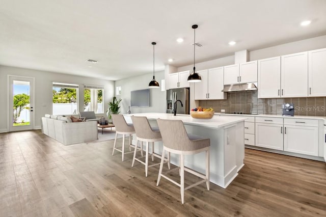4244 11th Ave N, Saint Petersburg, FL 33713 - kitchen with stainless steel refrigerator with ice dispenser, under cabinet range hood, backsplash, a kitchen bar, and wood finished floors