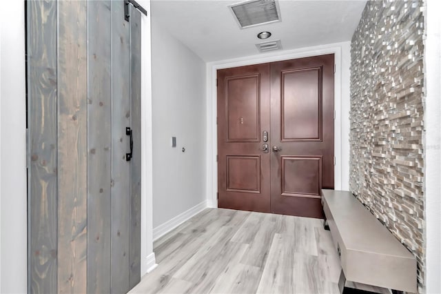 entrance foyer featuring a barn door, visible vents, light wood finished floors, and baseboards