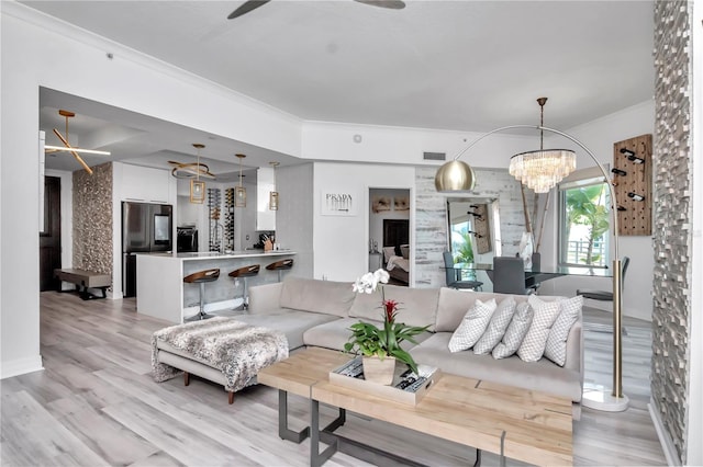 living area featuring light wood-style floors, visible vents, crown molding, and ceiling fan with notable chandelier