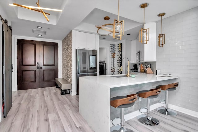 kitchen featuring a sink, light wood-style flooring, a peninsula, white cabinets, and appliances with stainless steel finishes