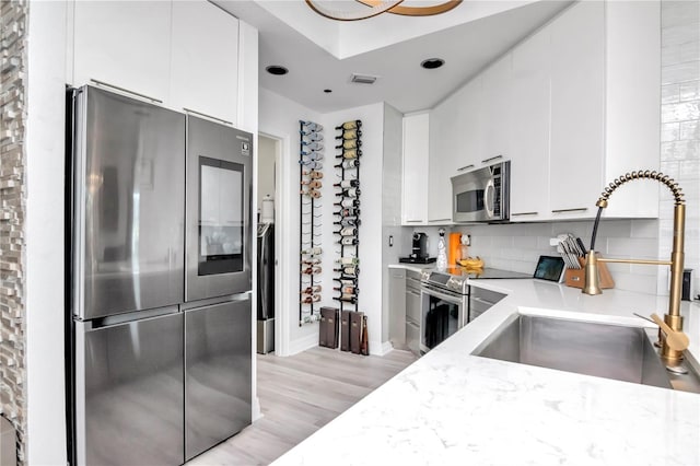 kitchen featuring decorative backsplash, stainless steel appliances, a sink, white cabinetry, and visible vents