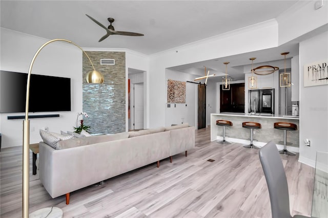 living area featuring a barn door, visible vents, ceiling fan, light wood-style floors, and ornamental molding