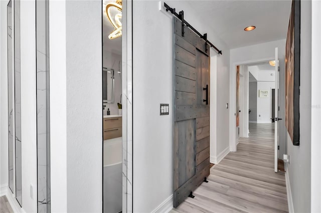 corridor with wood finished floors, a barn door, and baseboards