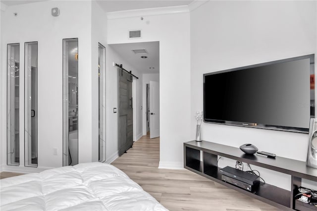bedroom with a barn door, visible vents, light wood-style flooring, and baseboards