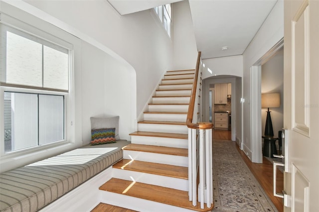 stairway featuring arched walkways and wood finished floors