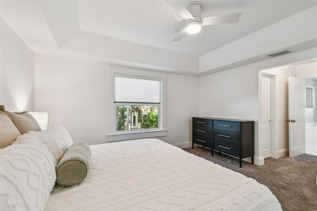 bedroom featuring visible vents, baseboards, a raised ceiling, dark carpet, and a ceiling fan