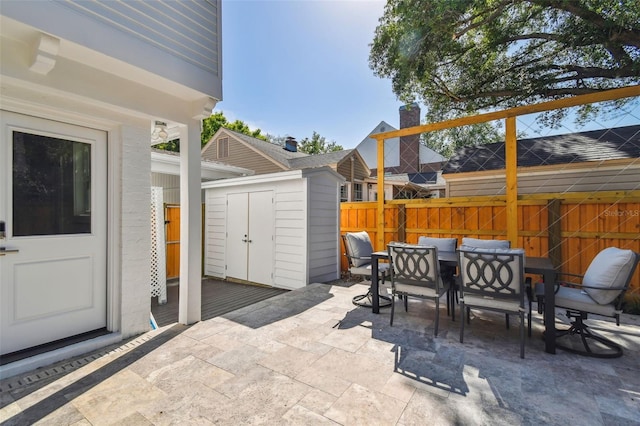 view of patio / terrace with an outdoor structure, outdoor dining space, fence, and a shed