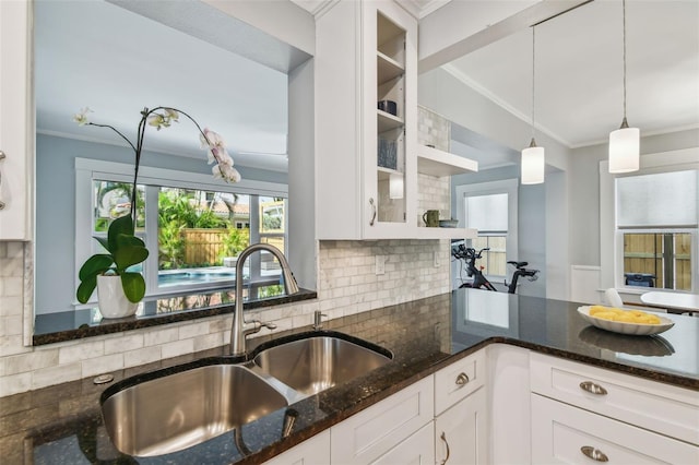 kitchen featuring dark stone countertops, glass insert cabinets, a sink, crown molding, and white cabinetry