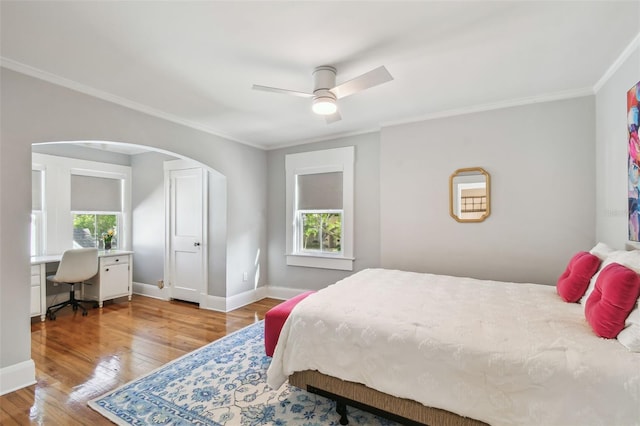 bedroom featuring arched walkways, crown molding, wood-type flooring, and multiple windows