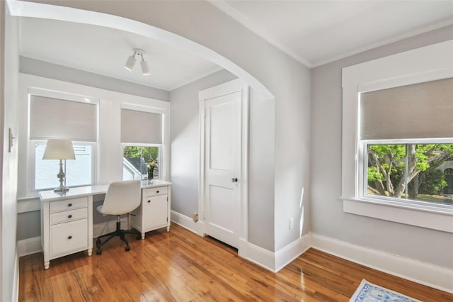 office space featuring crown molding, baseboards, light wood finished floors, and arched walkways