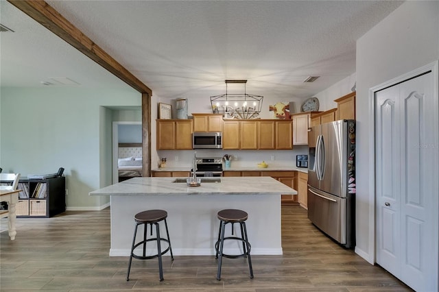 7511 Turtle View Dr, Ruskin, FL 33573 - kitchen featuring stainless steel appliances, a chandelier, a center island with sink, a kitchen bar, and wood finished floors