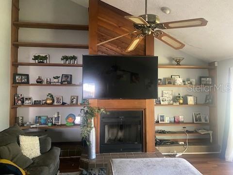living room with wood finished floors, a fireplace with raised hearth, a ceiling fan, and vaulted ceiling