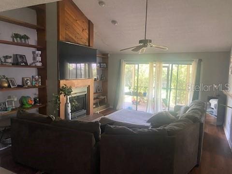 living room featuring built in shelves, dark wood-style flooring, ceiling fan, a fireplace, and vaulted ceiling